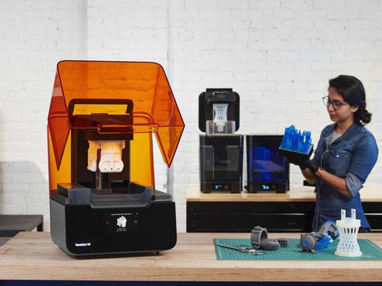 formlabs drucker links vorne, rechts hinten steht eine frau die sich ein gedrucktes teil anschaut