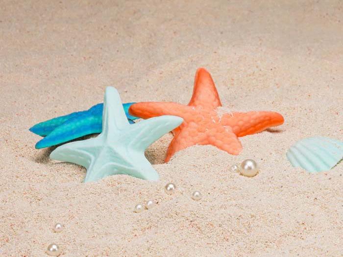 im sand liegen 3 sehsterne, in oranger, türkisblauer und hell blauer farbe